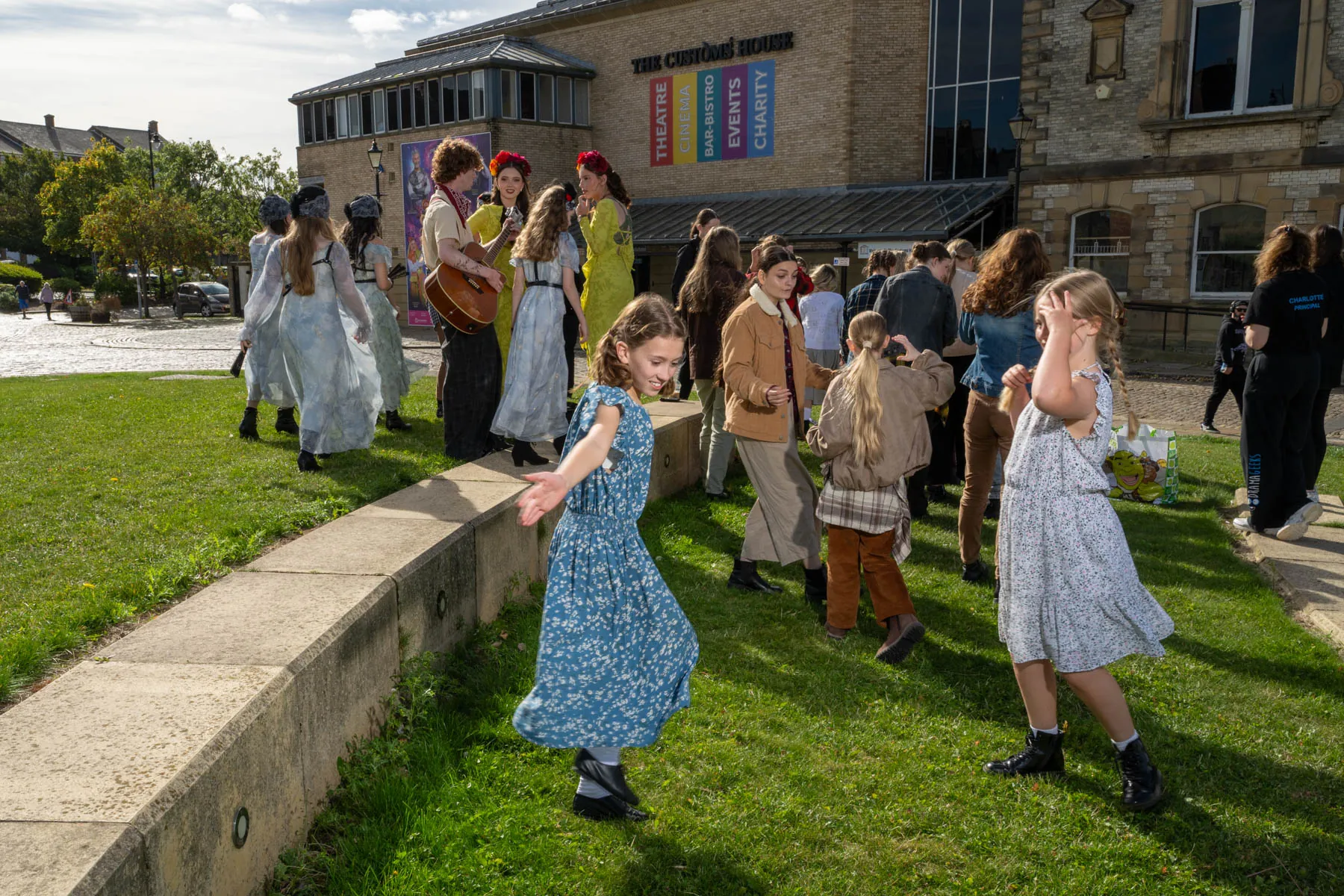 The Hadestown cast in costume dancing on the grass outside The Customs House